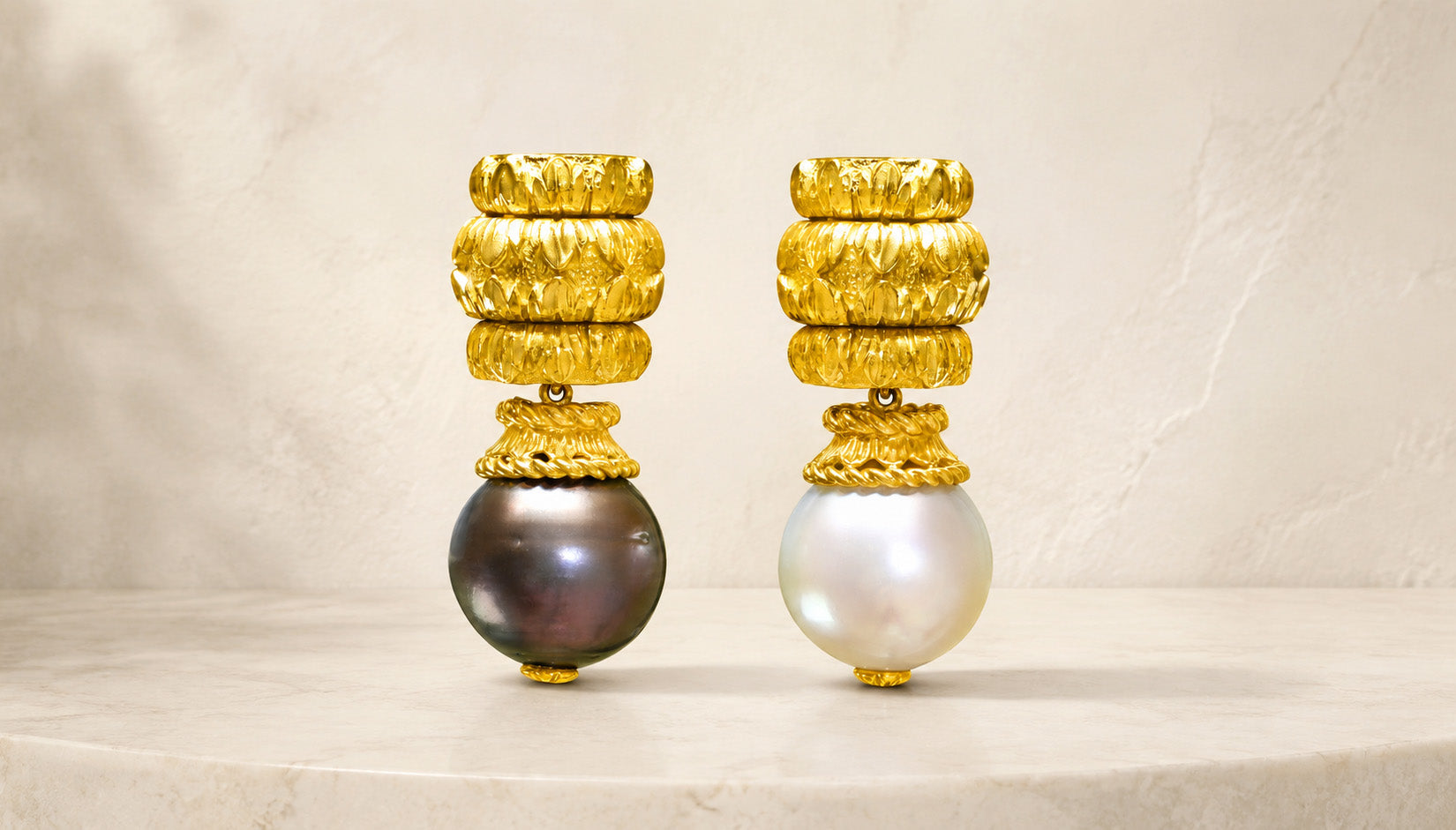 David Webb 18K yellow gold earrings with black and white pearls on an ivory stone background.