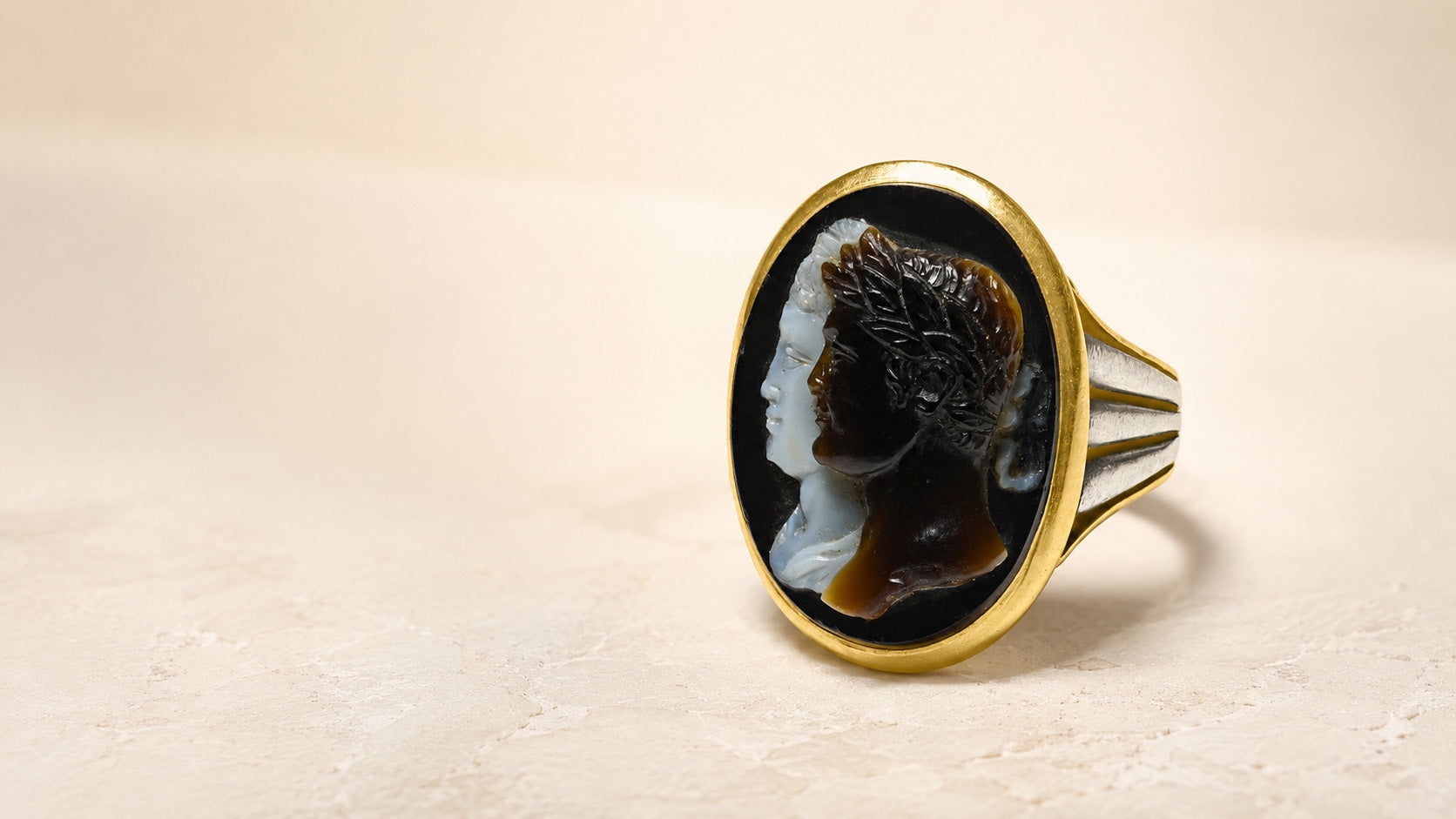 Antique Victorian cameo ring with two carved classical profiles, a gold bezel and silver-toned shoulders on an ivory background.