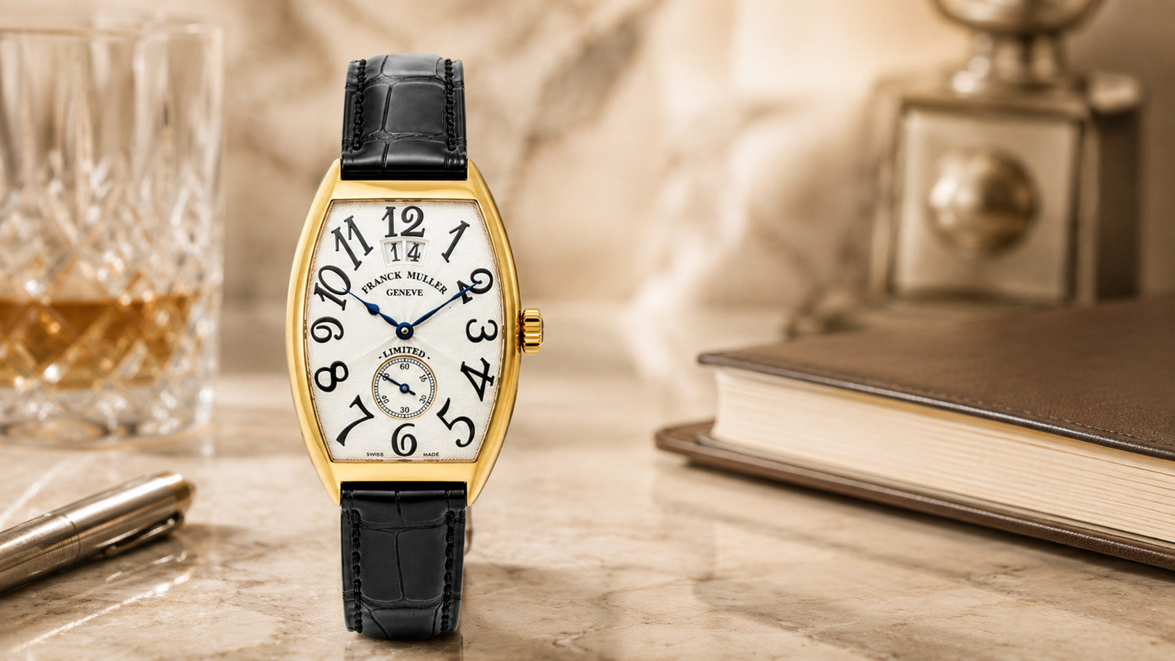 Franck Muller yellow gold wristwatch with black leather strap styled in an elegant editorial setting with a crystal glass, book, and pen, for DSF Antique Jewelry featured in The Good Men Project.