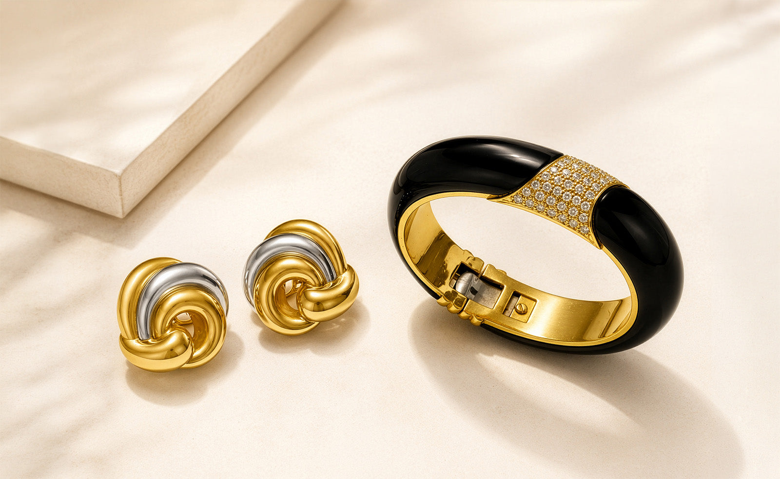 Signed designer earrings and onyx diamond bangle on an ivory background for DSF’s fine jewelry buying guide.